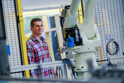 Produktionsteknolog_Uddannelse var hårdt men det helt rigtige Mandlig studerende på produktionsteknolog står i produktionsvirksomhed. I forgrunden står en robot